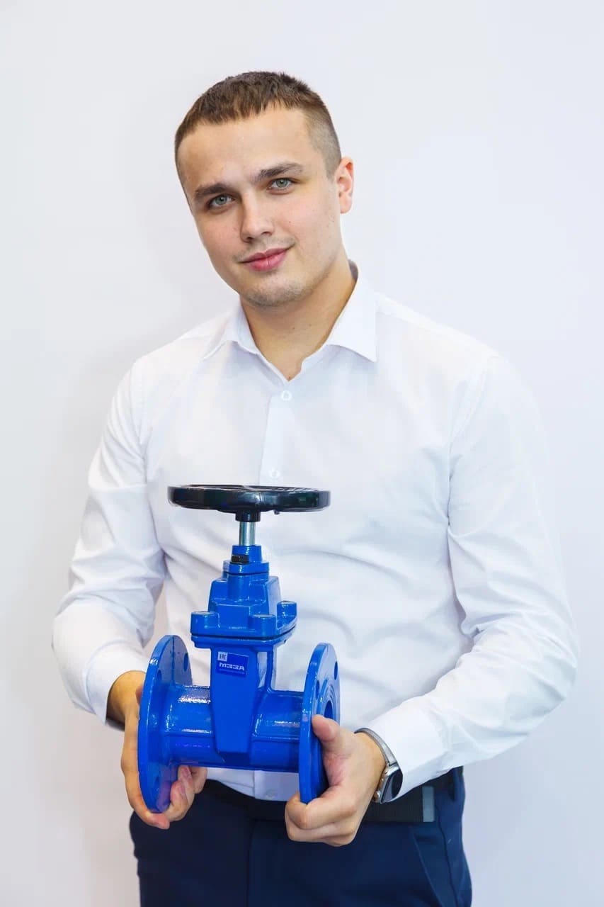 Мужчина в белой рубашке держит в руках клиновую чугунную задвижку